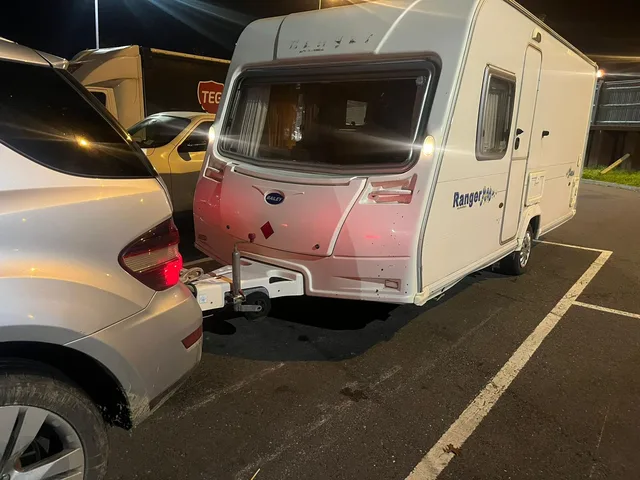 Touring caravan and tow vehicle in a marked car park after dark