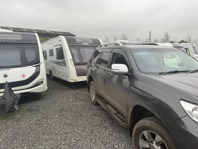 Rows of touring caravans beside a tow vehicle in a gravel yard