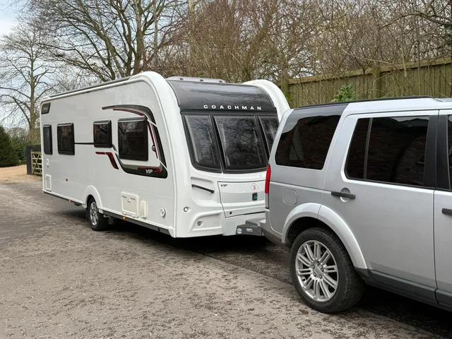 Touring caravan and tow vehicle beside trees and fencing